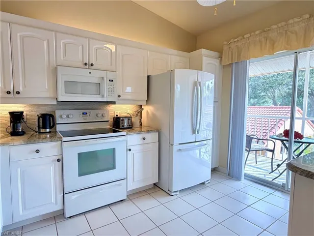 Kitchen featuring white appliances, white cabinets, light stone counters, backsplash, and vaulted ceiling