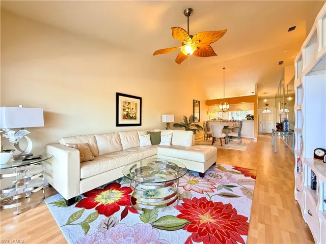 Living room with ceiling fan, light wood-style flooring, vaulted ceiling, and a chandelier