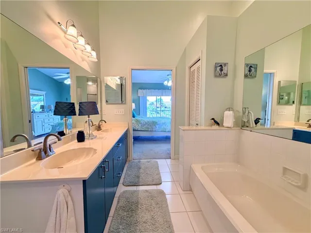 Full bath featuring ensuite bath, double vanity, a bath, light tile patterned flooring, and a closet