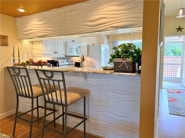 Kitchen featuring white cabinetry, light stone counters, white appliances, light wood-style floors, and a kitchen bar