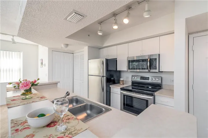 Kitchen featuring sink, appliances with stainless steel finishes, rail lighting,  and white cabinets