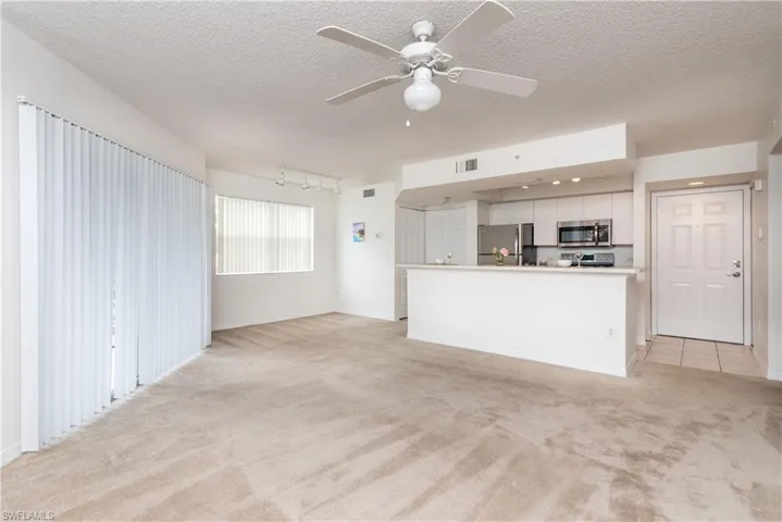 Unfurnished living room with light colored carpet, track lighting, and ceiling fan