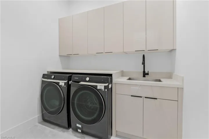 Clothes washing area with sink, cabinets, washer and dryer, and light tile patterned flooring