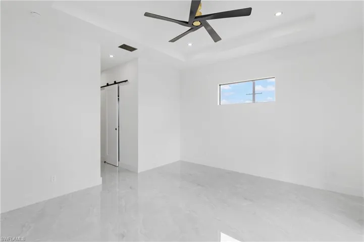 Tiled spare room with ceiling fan, a tray ceiling, and a barn door