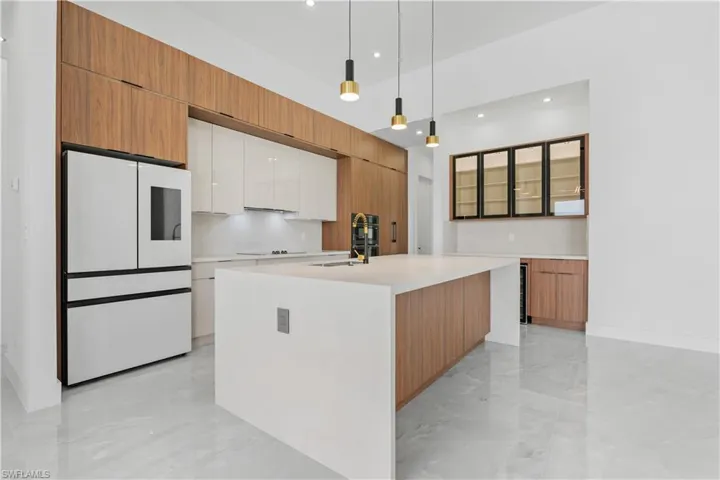 Kitchen featuring white appliances, sink, pendant lighting, an island with sink, and wine cooler