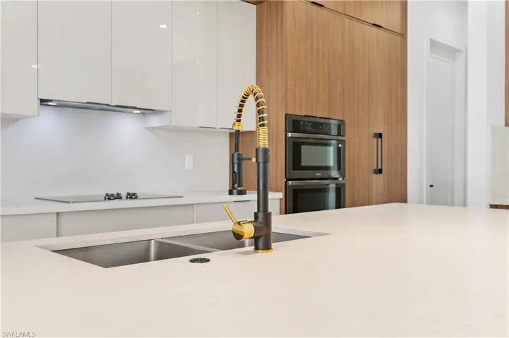 Kitchen featuring white cabinetry, light brown cabinetry, sink, and multiple ovens