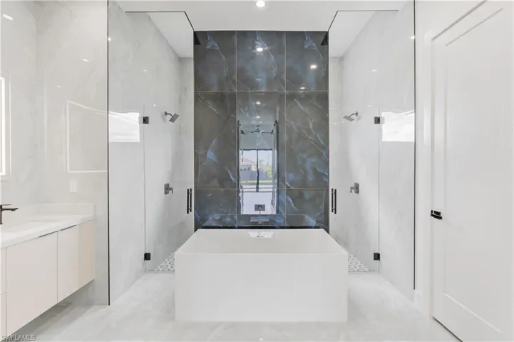 Bathroom featuring tile patterned floors, a shower with shower door, vanity, and tile walls