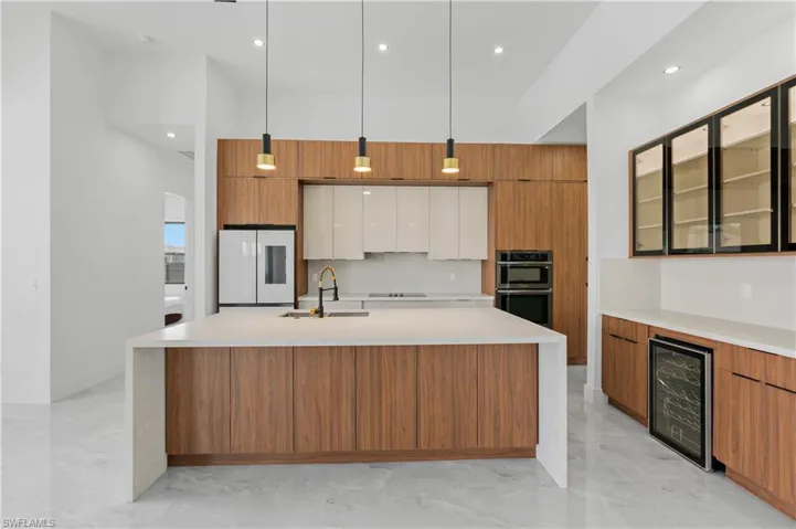 Kitchen featuring white refrigerator, sink, multiple ovens, a center island with sink, and wine cooler