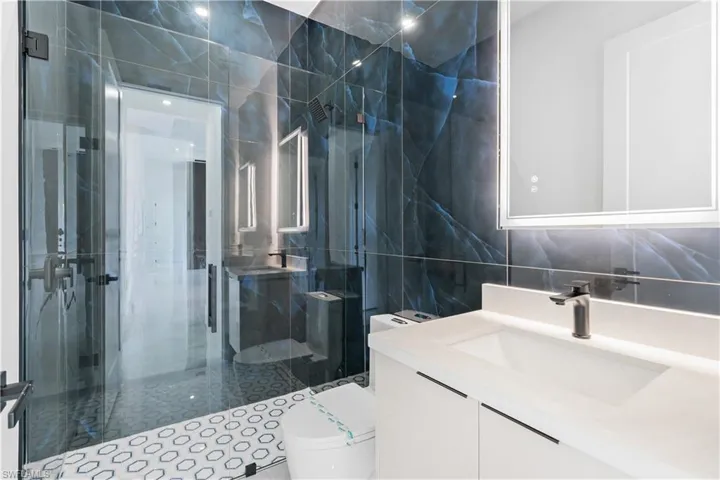 Bathroom featuring a shower with door, vanity, tile walls, and toilet