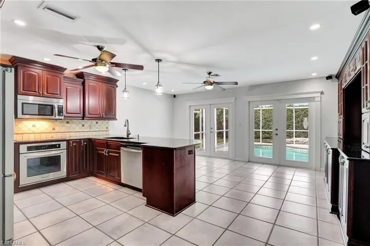 Kitchen with french doors,  wood finish cabinets, hanging light fixtures, stainless steel appliances, and decorative backsplash.