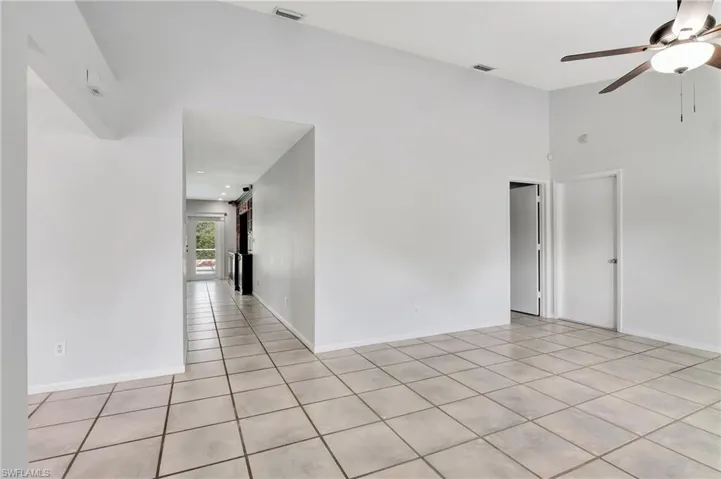 Living room with ceiling fan, light tile patterned floors, and a high ceiling.