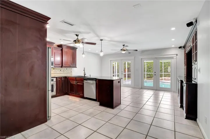 Kitchen with French doors, wood finish cabinets, a peninsula, decorative backsplash, and stainless steel appliances.