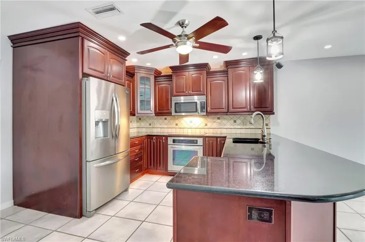 Kitchen featuring stainless steel appliances, bold wood finish cabinetry, pendant lighting, a peninsula, and dark stone counters.