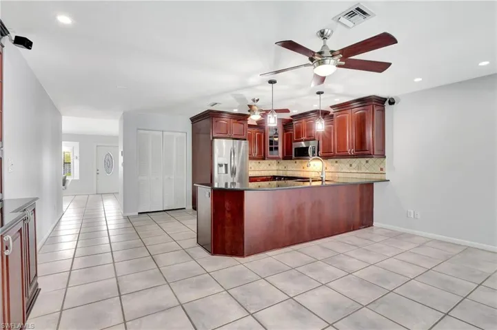 Kitchen featuring wood finish cabinetry, a peninsula, stainless steel appliances, dark stone counters, and decorative backsplash.