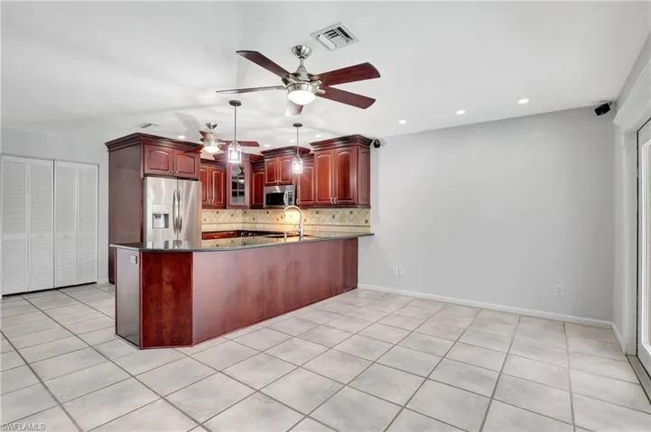 Kitchen featuring cherry color  cabinets, stainless steel appliances, a peninsula, dark stone countertops, and decorative backsplash