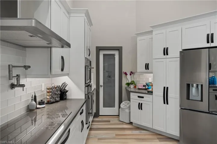 Kitchen featuring wall chimney range hood, appliances with stainless steel finishes, white cabinets, and a large walk-in pantry