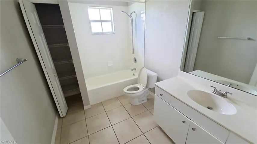 Bathroom featuring a single vanity with an integrated sink, a large wall-mounted mirror, a bathtub with an overhead shower, and neutral floor tiling