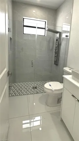 Bathroom with a shower with shower door, toilet, vanity, tile walls, and tile patterned floors