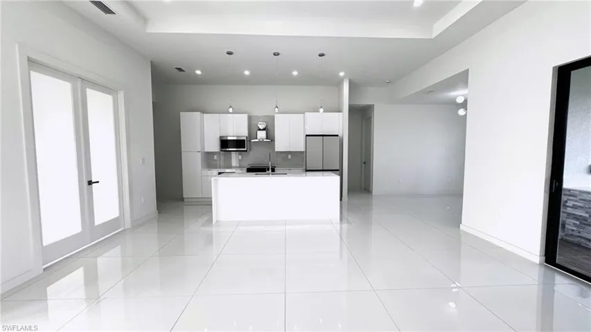 Kitchen featuring hanging light fixtures, stainless steel appliances, light tile patterned floors, and an island with sink