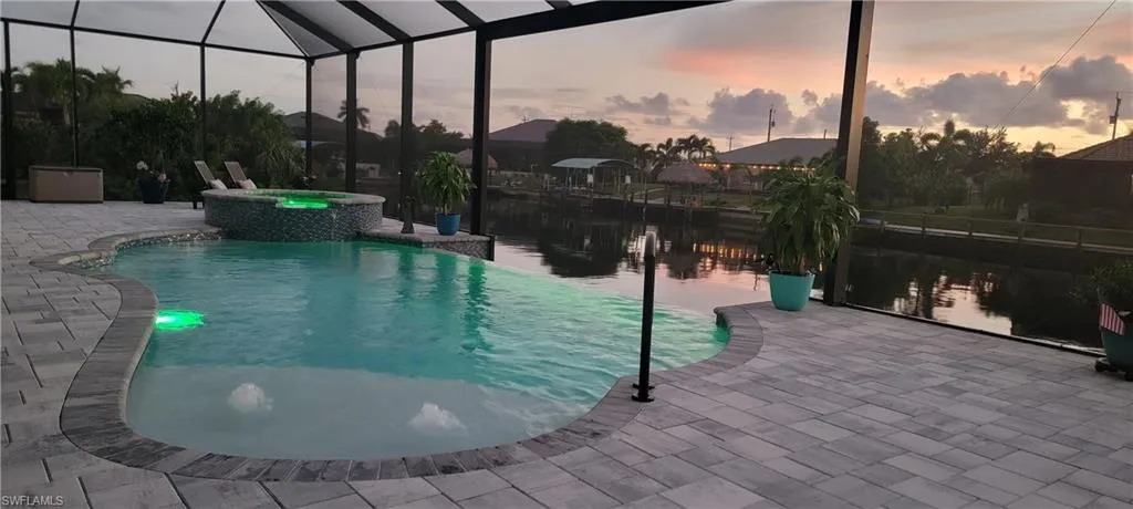 Pool at dusk with glass enclosure, an in ground hot tub, and a patio