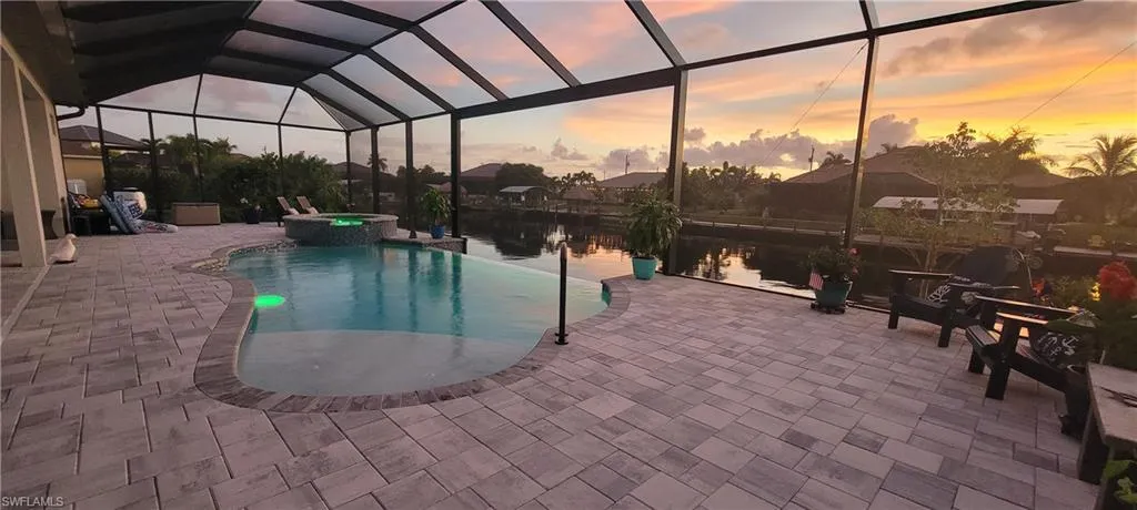 Pool at dusk with glass enclosure, an in ground hot tub, and a patio area