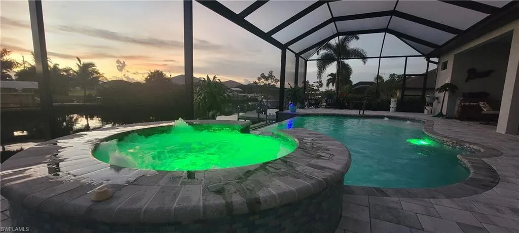 Pool at dusk featuring glass enclosure and a patio