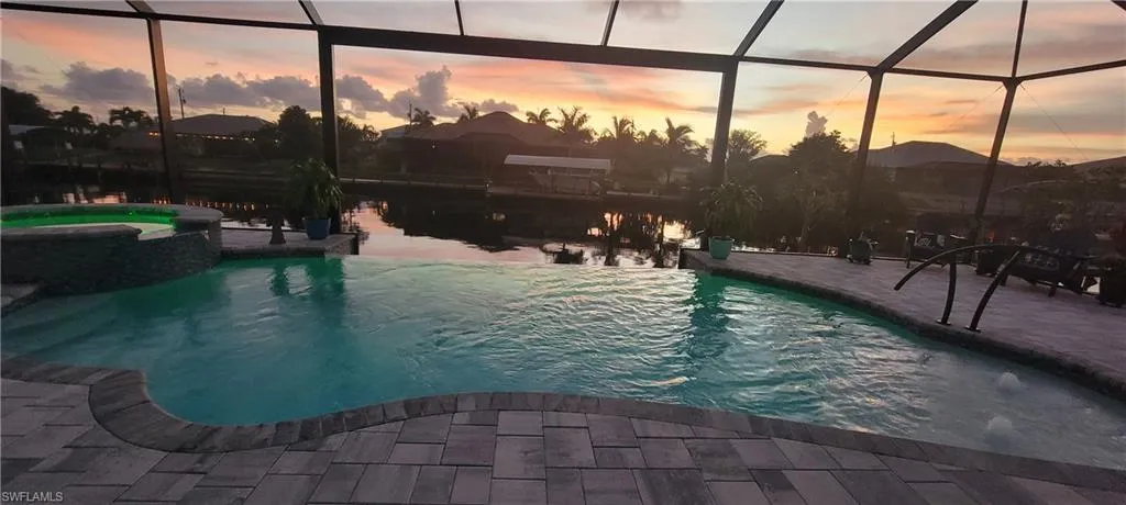 Pool at dusk featuring glass enclosure and a patio
