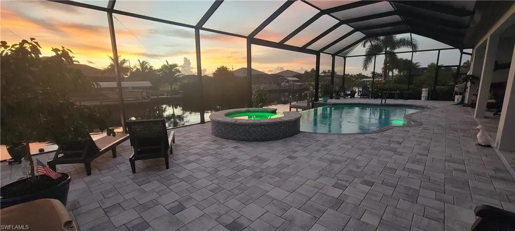Pool at dusk with glass enclosure, an in ground hot tub, and a patio area