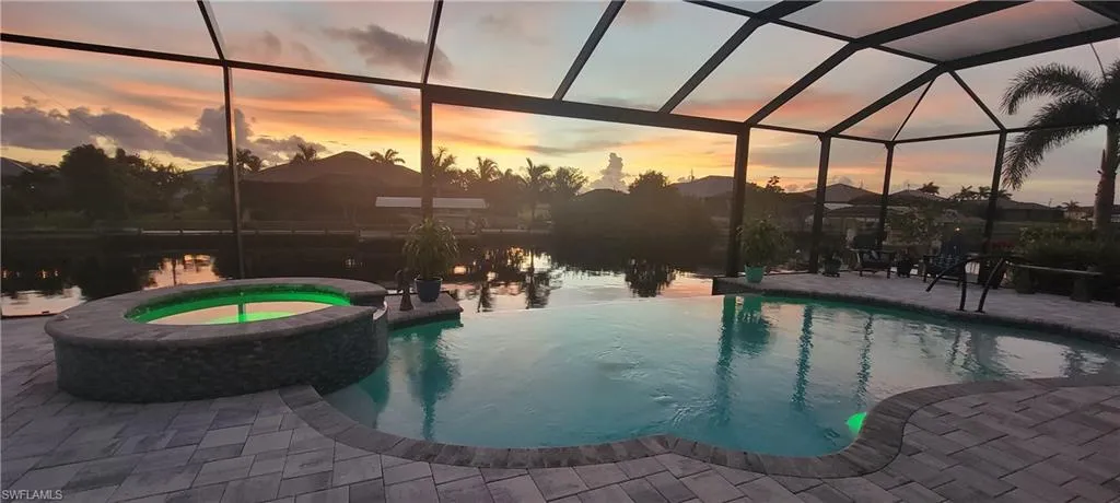 Pool at dusk with a lanai, a patio, and an in ground hot tub