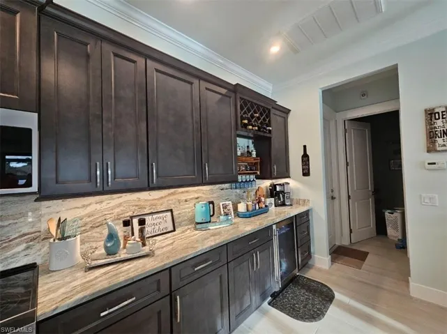 Kitchen with tasteful backsplash, light stone counters, crown molding, and dark brown cabinetry