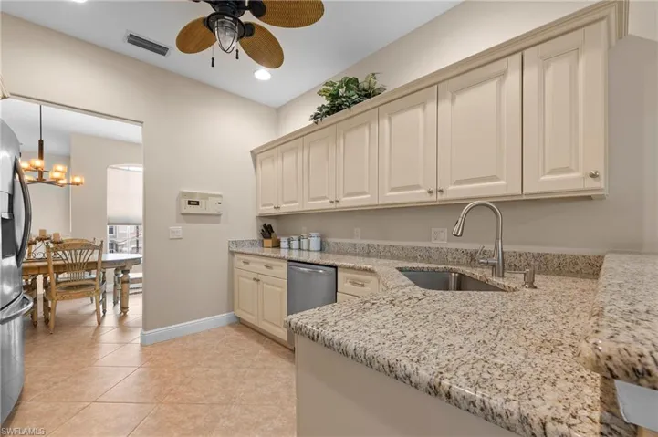 Kitchen featuring light tile patterned floors, decorative light fixtures, ceiling fan with notable chandelier, light stone counters, and sink