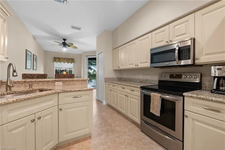 Kitchen with cream cabinets, light stone countertops, stainless steel appliances, sink, and ceiling fan