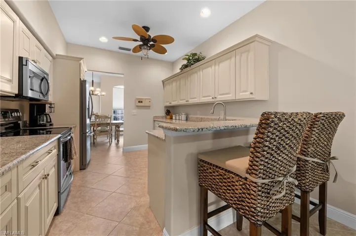 Kitchen with ceiling fan with notable chandelier, appliances with stainless steel finishes, light stone counters, and a breakfast bar