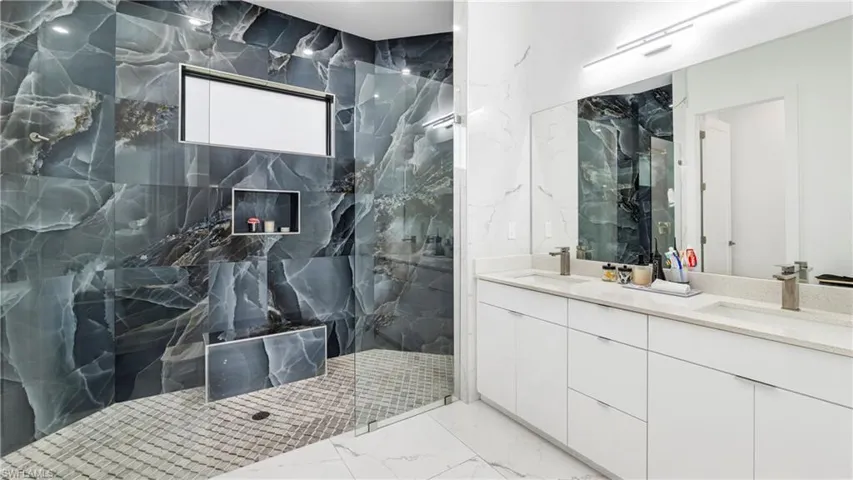 Bathroom featuring double vanity, a marble finish shower, stone wall, and light marble finish flooring