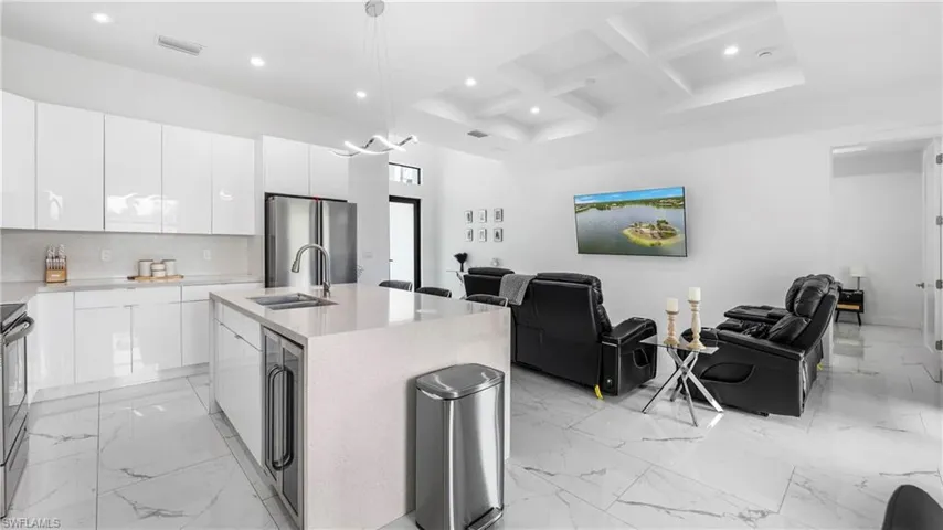 Kitchen with open floor plan, coffered ceiling, an island with sink, beverage cooler, and stainless steel appliances