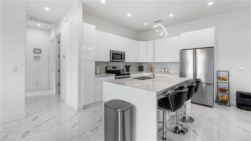 Kitchen featuring stainless steel appliances, modern cabinets, a center island with sink, and white cabinetry