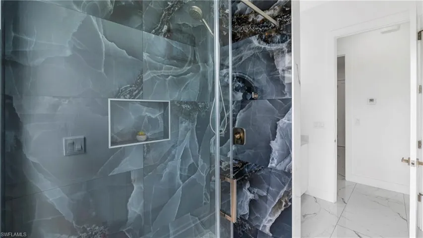 Full bath featuring a marble finish shower and light marble finish flooring