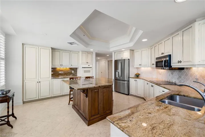 Kitchen with light stone counters, stainless steel fridge with ice dispenser, backsplash, a raised ceiling, and recessed lighting