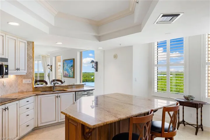 Kitchen featuring light stone countertops, a kitchen breakfast bar, decorative backsplash, ornamental molding, and a tray ceiling
