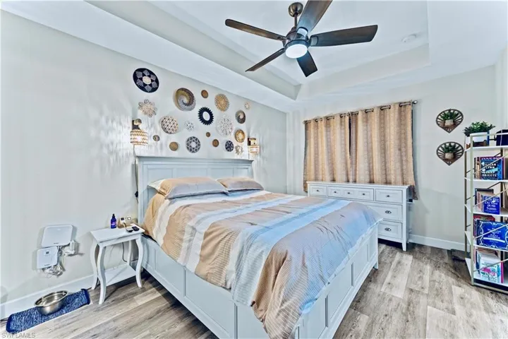 Bedroom with baseboards, a ceiling fan, a tray ceiling, and light wood-type flooring