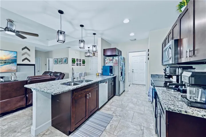 Kitchen featuring a peninsula, a sink, open floor plan, light stone countertops, and appliances with stainless steel finishes