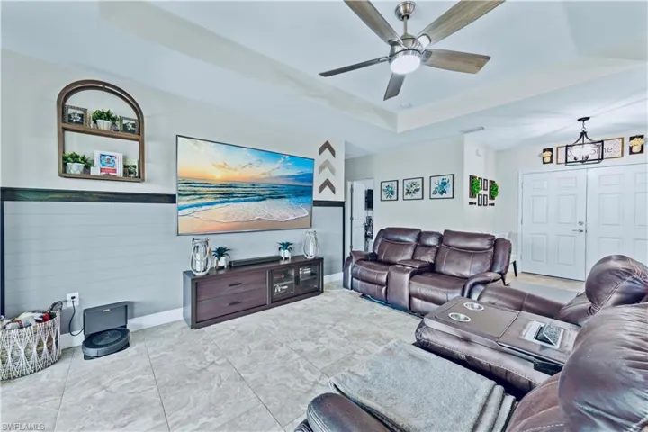 Living room featuring baseboards, ceiling fan with notable chandelier, and a raised ceiling