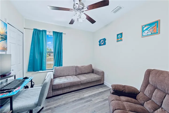 Living room with wood finished floors, visible vents, baseboards, and ceiling fan