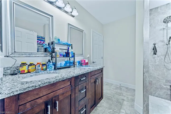 Bathroom with marble finish floor, walk in shower, a sink, and double vanity
