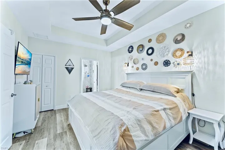 Bedroom featuring ceiling fan, a tray ceiling, and light wood-type flooring