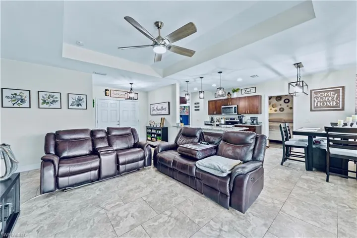 Living room featuring a raised ceiling, a ceiling fan, and baseboards