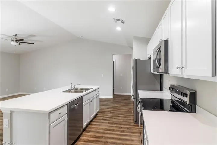 Kitchen with stainless steel appliances, dark wood-style flooring, ceiling fan, a center island with sink, and white cabinetry