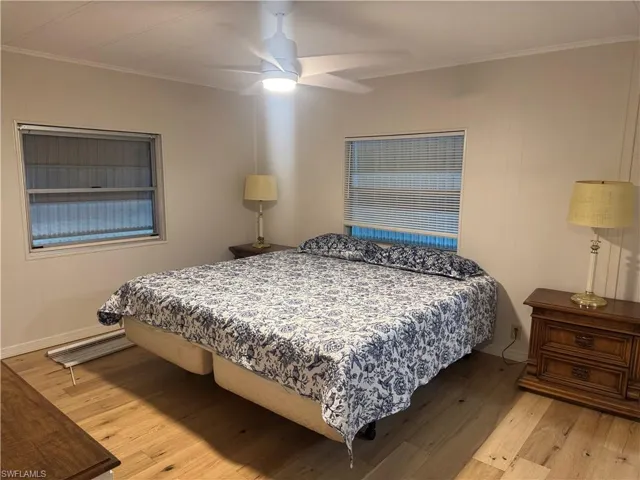 Room featuring wood-finish flooring, two windows with blinds, and a ceiling fan with integrated lighting
