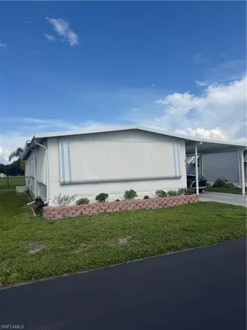 White exterior siding with blue striped awnings, an attached carport, and a decorative brick-lined planting bed