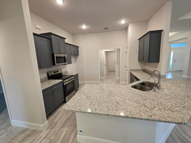 Kitchen with light stone countertops, appliances with stainless steel finishes, sink, kitchen peninsula, and light hardwood / wood-style flooring